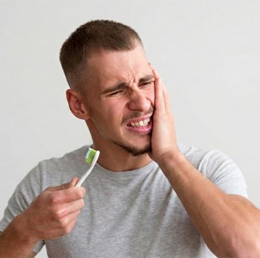 Hombre con dolor de muelas sosteniendo un cepillo de dientes, dentista de Pearly Whites de Pearland.