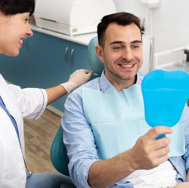 La Dra. Paola Argaez, dentista de habla hispana en Pearland, con un paciente sonriente sosteniendo un espejo.